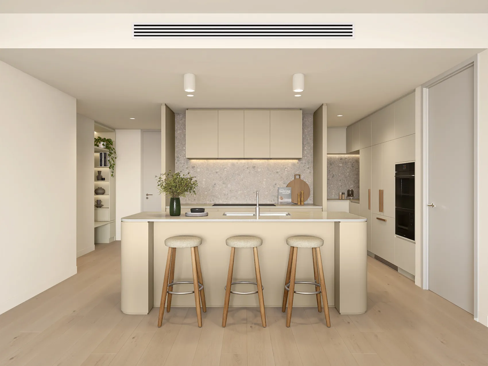 Modern kitchen with beige cabinetry, an island with a sink, two padded wooden bar stools, and a vase of green foliage.