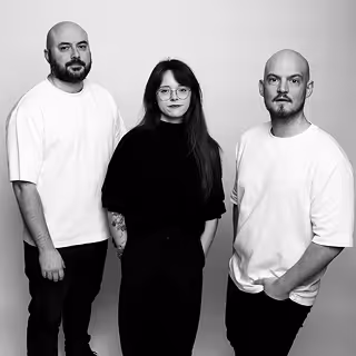 Portrait en noir et blanc de deux hommes et une femme debout, tous habillés de manière décontractée avec des expressions neutres.