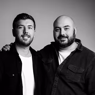 Portrait en noir et blanc de deux hommes souriants, l’un avec une barbe et l’autre avec la main posée sur l’épaule de l’autre.