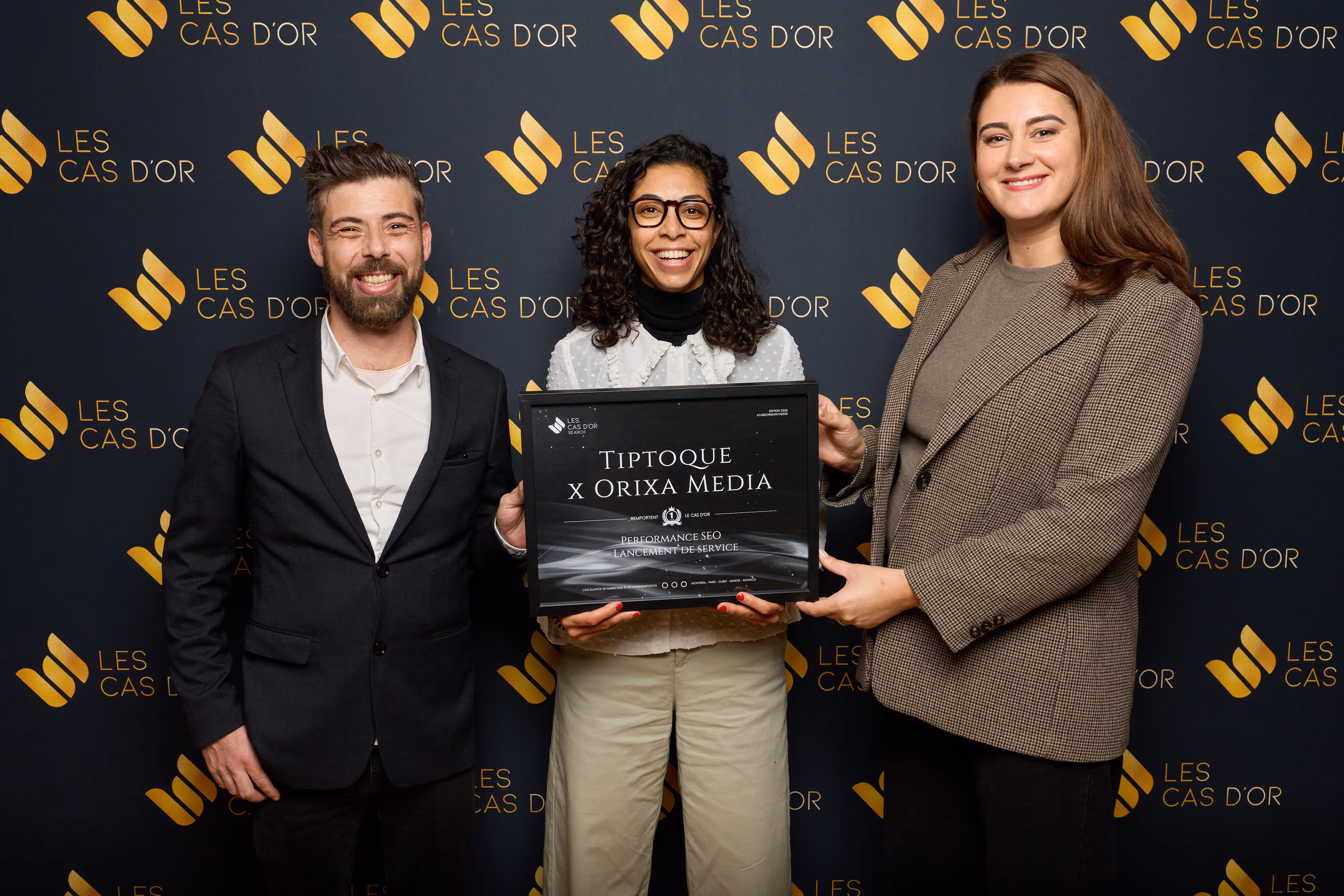 Trois personnes souriantes tenant un trophée de récompense Tiptoque x Orixa Media pour performance SEO.