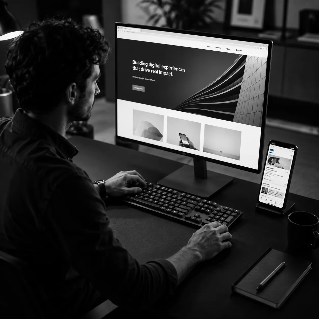 Person working on a computer with a smartphone and notebook on the desk.