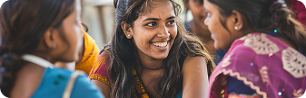Smiling young woman engaging in conversation with two other women, all wearing traditional colorful clothing.