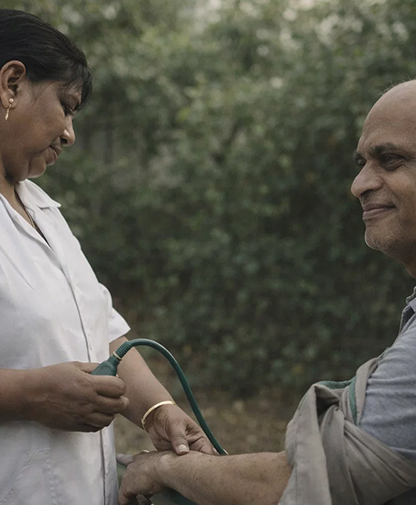 Healthcare worker measuring blood pressure on a smiling elderly man's arm outdoors.