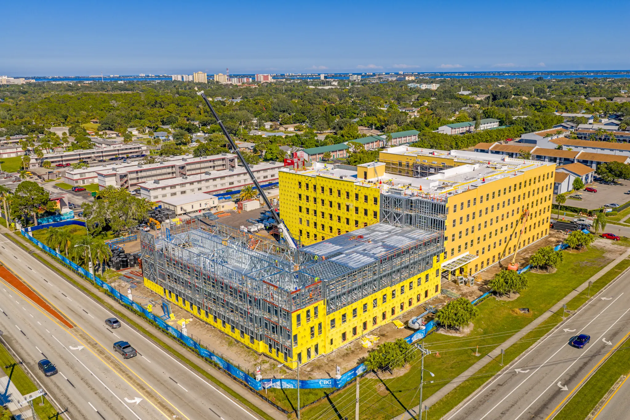 Aerial view of a large yellow building under construction with steel framework and cranes on a sunny day.