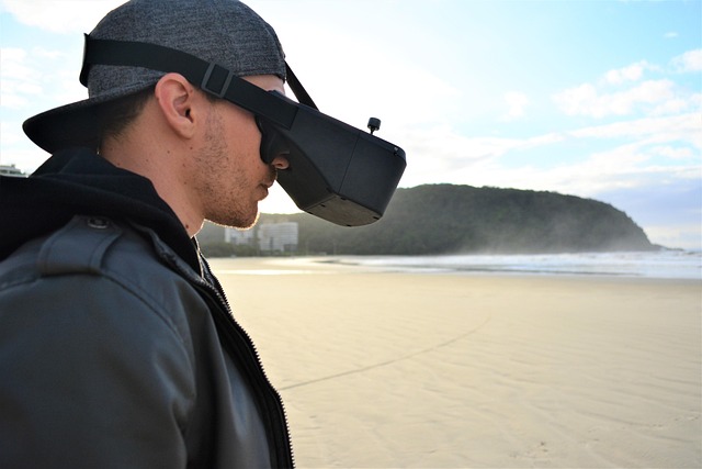 Homme sur une plage portant un casque de réalité virtuelle avec vue sur la mer et une colline.
