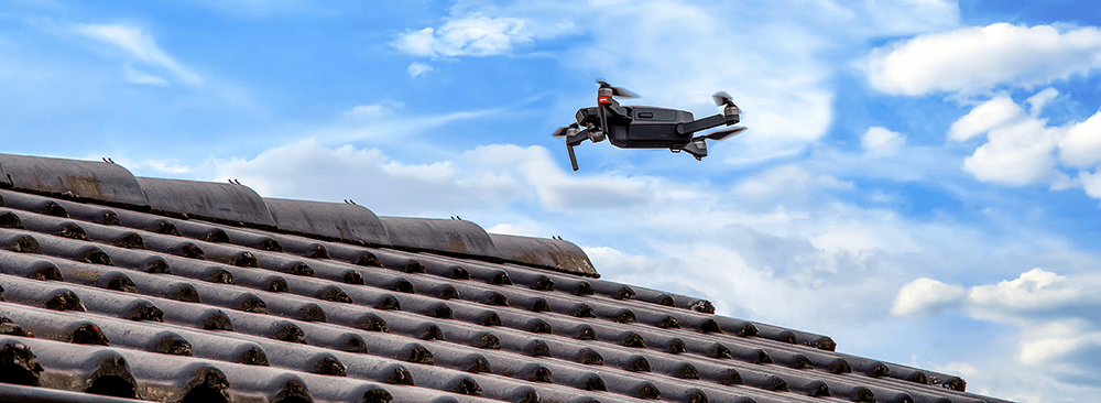 Un drone volant au-dessus d'un toit en tuiles sous un ciel bleu avec quelques nuages blancs.