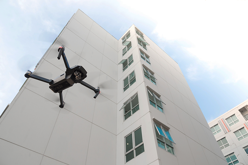 Un drone volant près d'un grand bâtiment moderne blanc avec plusieurs fenêtres ouvertes.