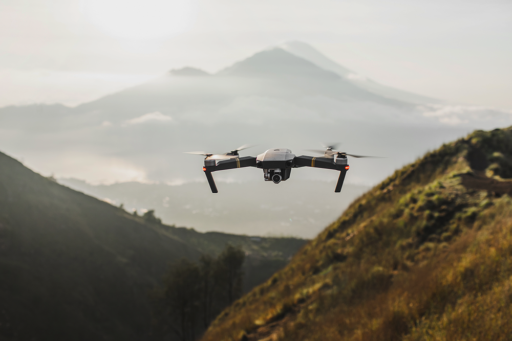 Drone volant entre des collines avec des montagnes brumeuses en arrière-plan.