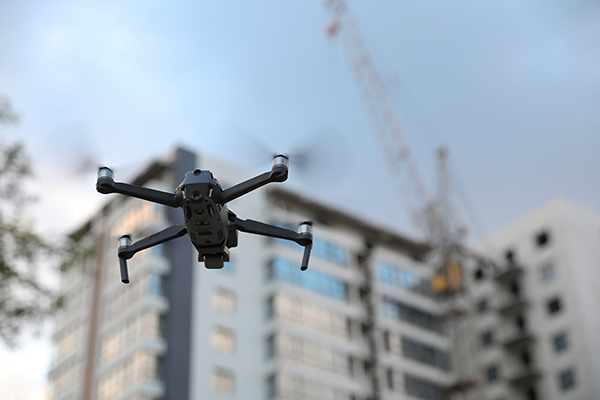 Drone volant devant un bâtiment en construction avec une grue au fond.