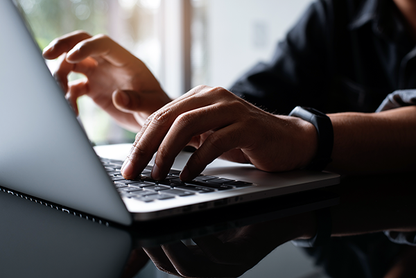 Personne tapant sur un clavier d'ordinateur portable dans un environnement lumineux près d'une fenêtre.
