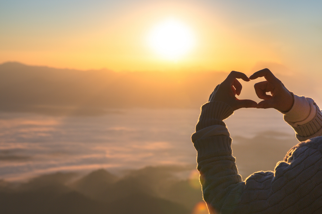 Hands forming a heart towards the sun, representing love, family and inherited conditions