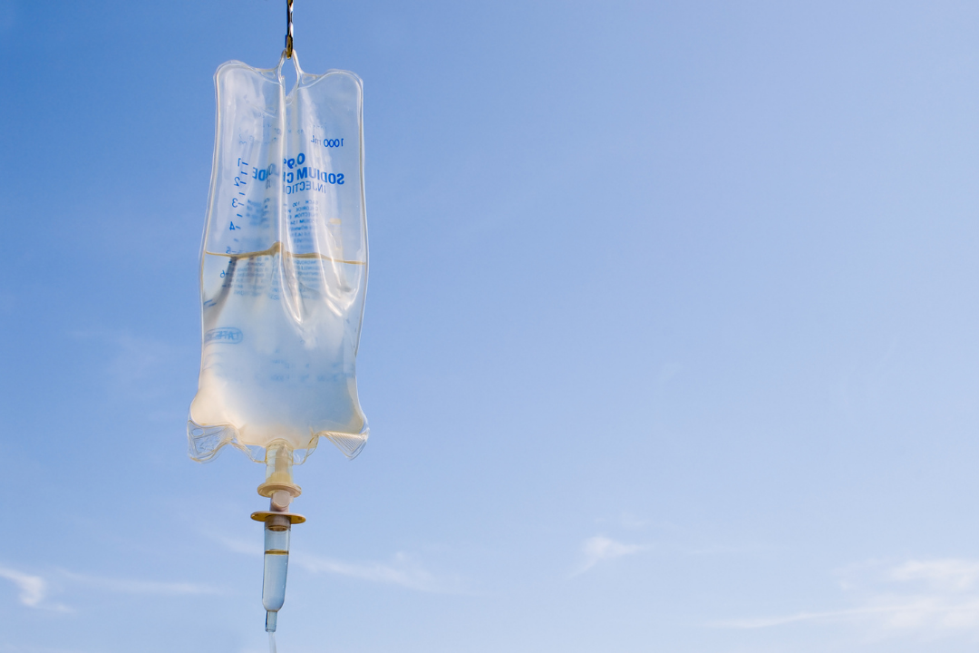 Intravenous IV fluid drip bag against a blue sky, representing hospital treatment and changing approaches to IV fluids in sickle cell pain crises and vaso-occlusive crisis management.