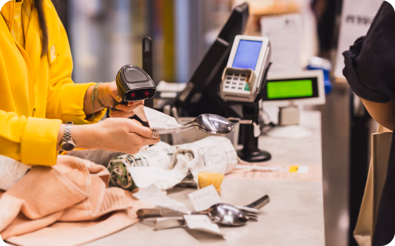 Cashier scanning a receipt wrapped around a spoon at a checkout counter with payment terminals in the background.