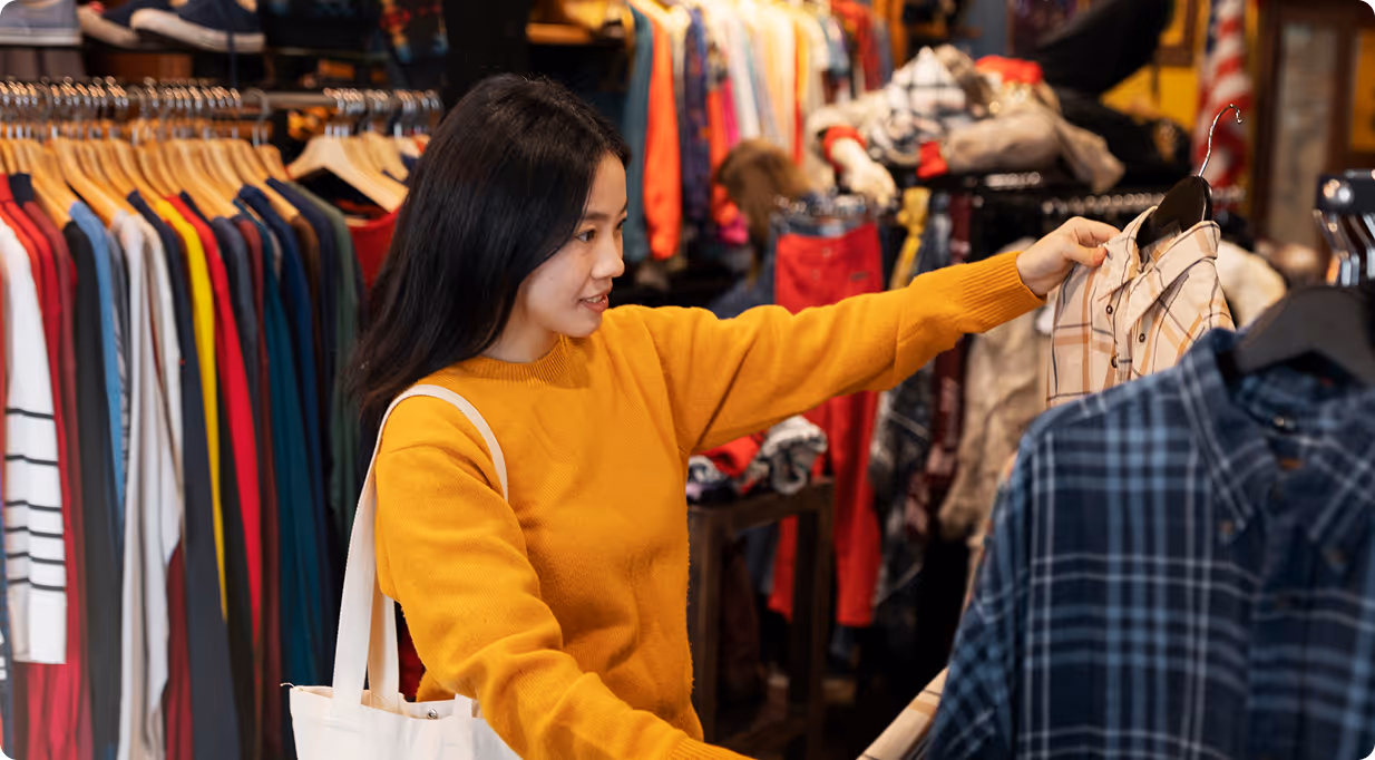Woman in a mustard sweater shopping for shirts in a clothing store.