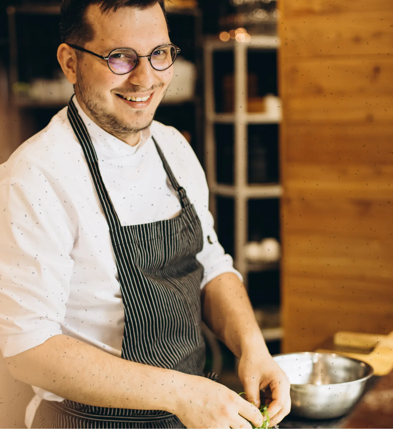 Smiling chef wearing glasses and a striped apron preparing food in a kitchen.