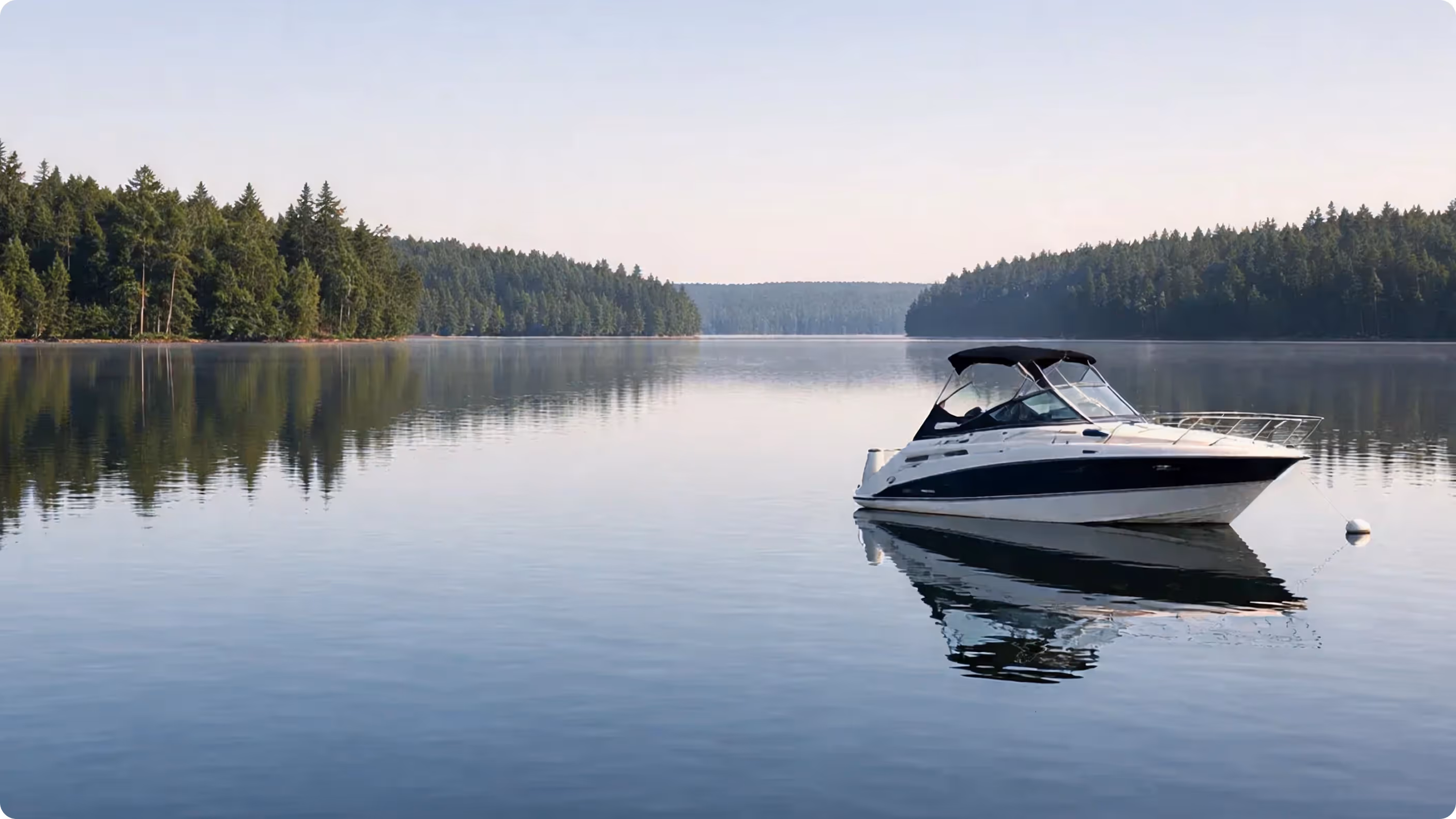 White and black motorboat anchored on calm lake with pine tree reflections and clear sky.