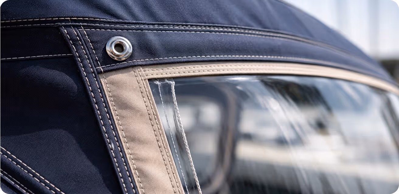 Close-up of a navy and beige fabric with clear plastic window and metal grommet, part of a vehicle's convertible top.