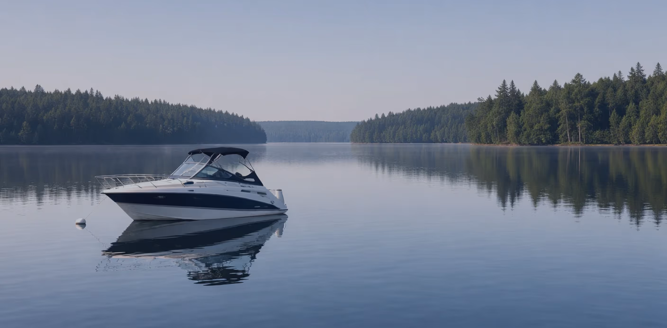 White and black motorboat anchored on calm lake with forested shorelines reflected in the water.