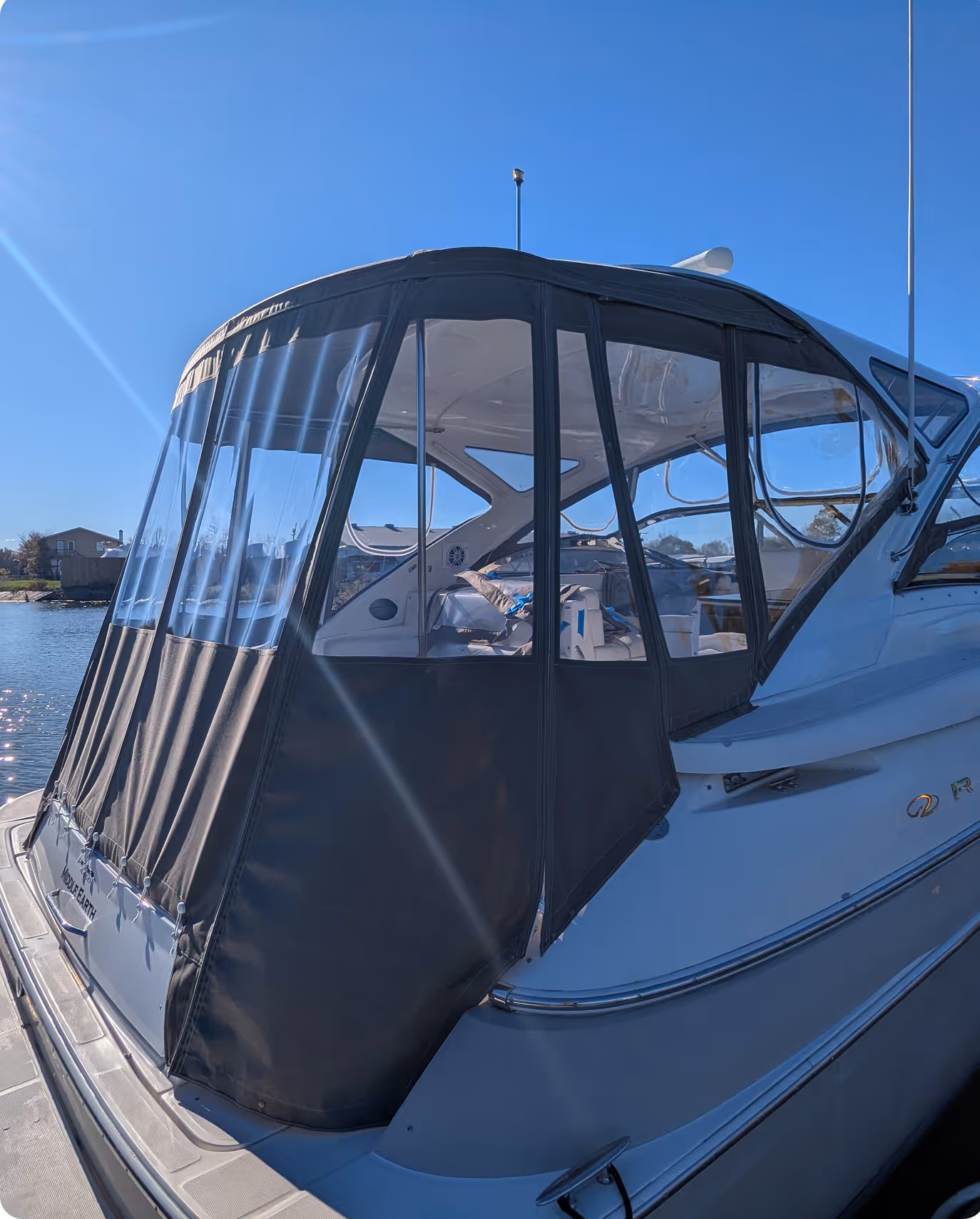 White motorboat docked with a black canvas enclosure covering its rear deck under a clear blue sky.