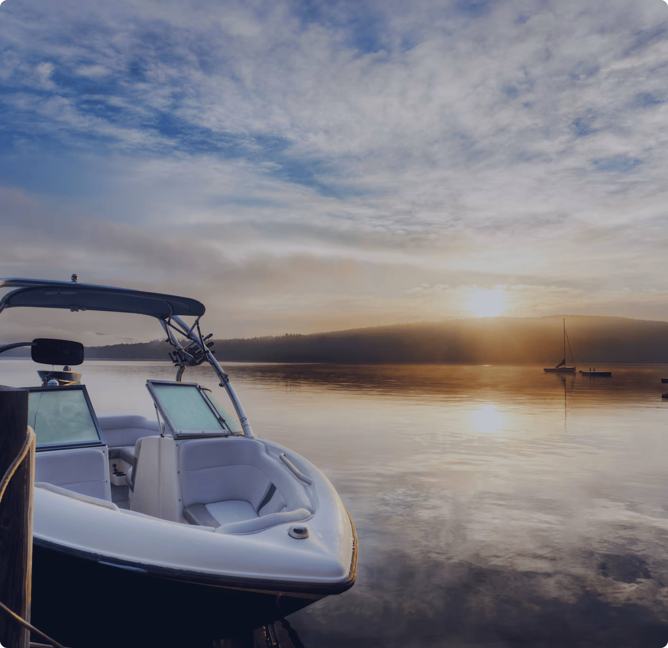 White boat docked on calm water at sunrise with a distant sailboat and hills under a cloudy sky.