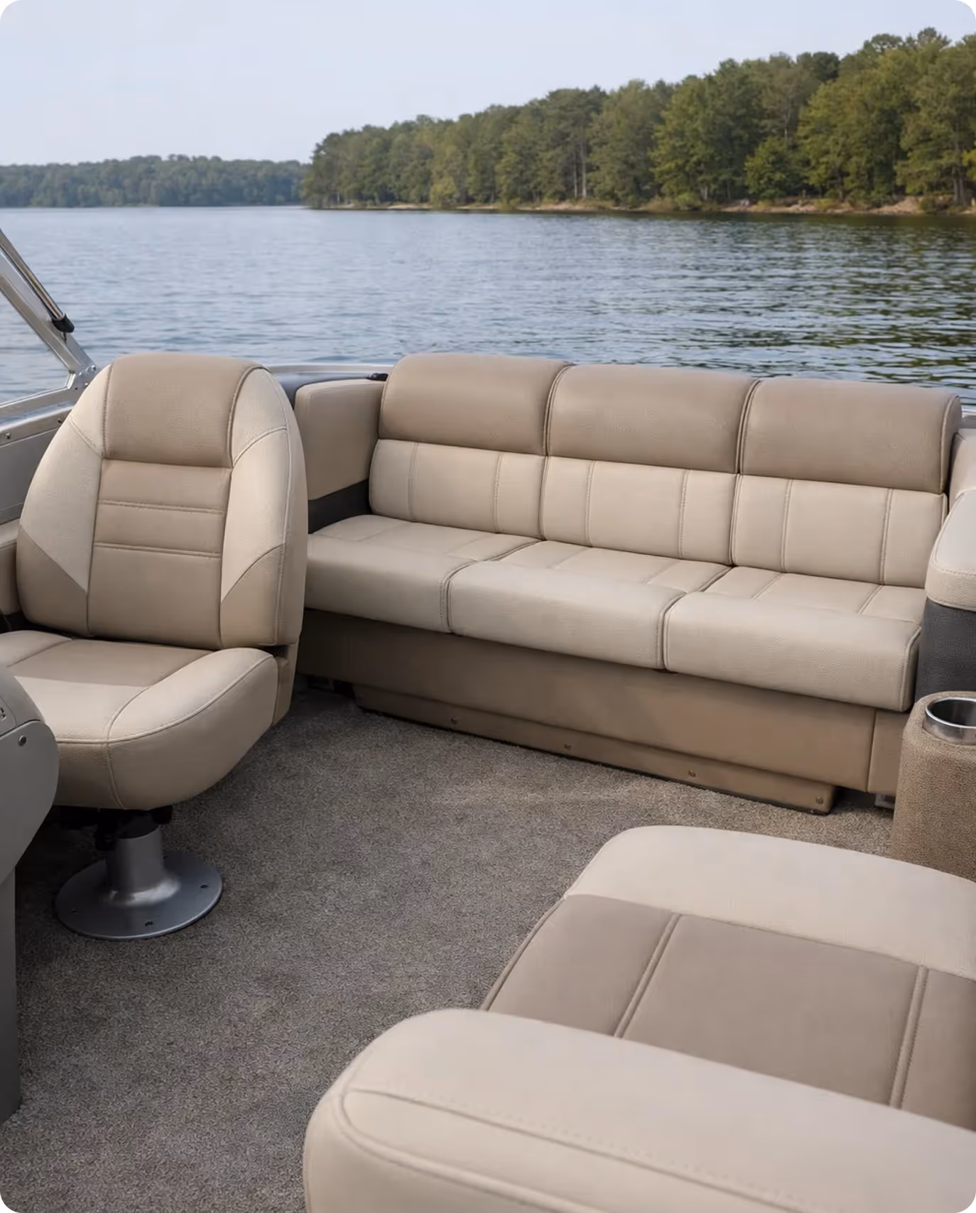 Interior seating area of a boat with beige cushioned seats and a view of a lake with trees in the background.