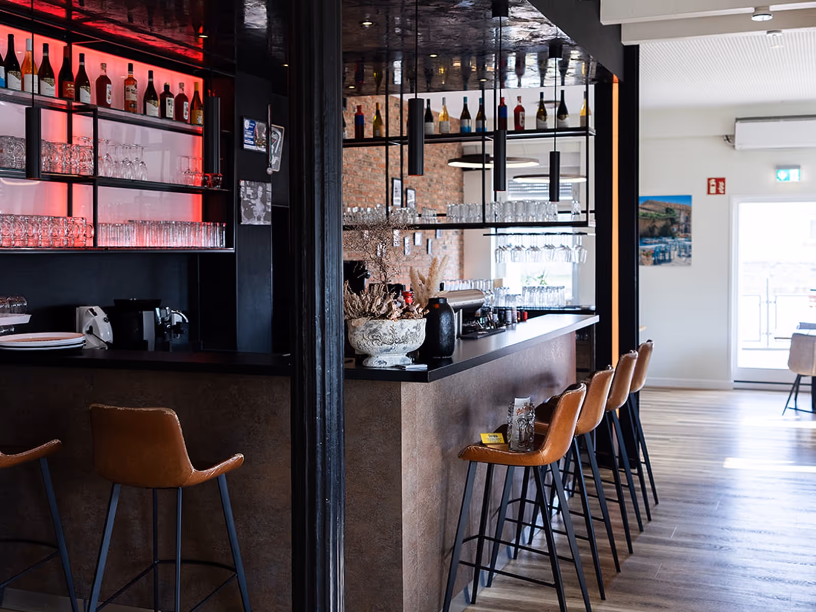 Innenansicht einer Bar mit einer Theke, fünf Leder-Barhockern und Regalen mit alkoholischen Getränken und Gläsern.