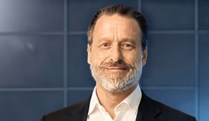 Man med skägg i kostym mot blå vägg, professionell porträttfoto.