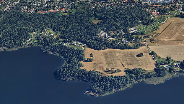 Flygfoto över jordbrukslandskap med åkrar, skogar och sjö. Lantbruk vid vattnet.