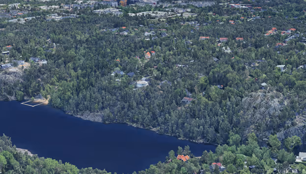 Flygfoto över skogsklädda område med djup sjö och spridda bostadshus