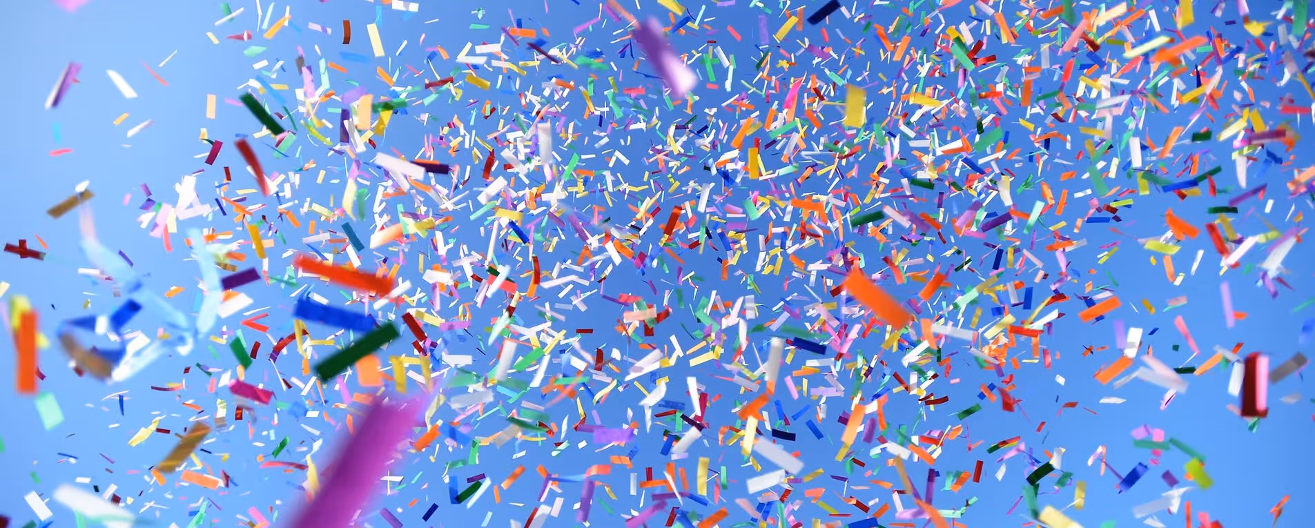 Bunte Konfetti fliegt vor blauem Himmel verteilt.