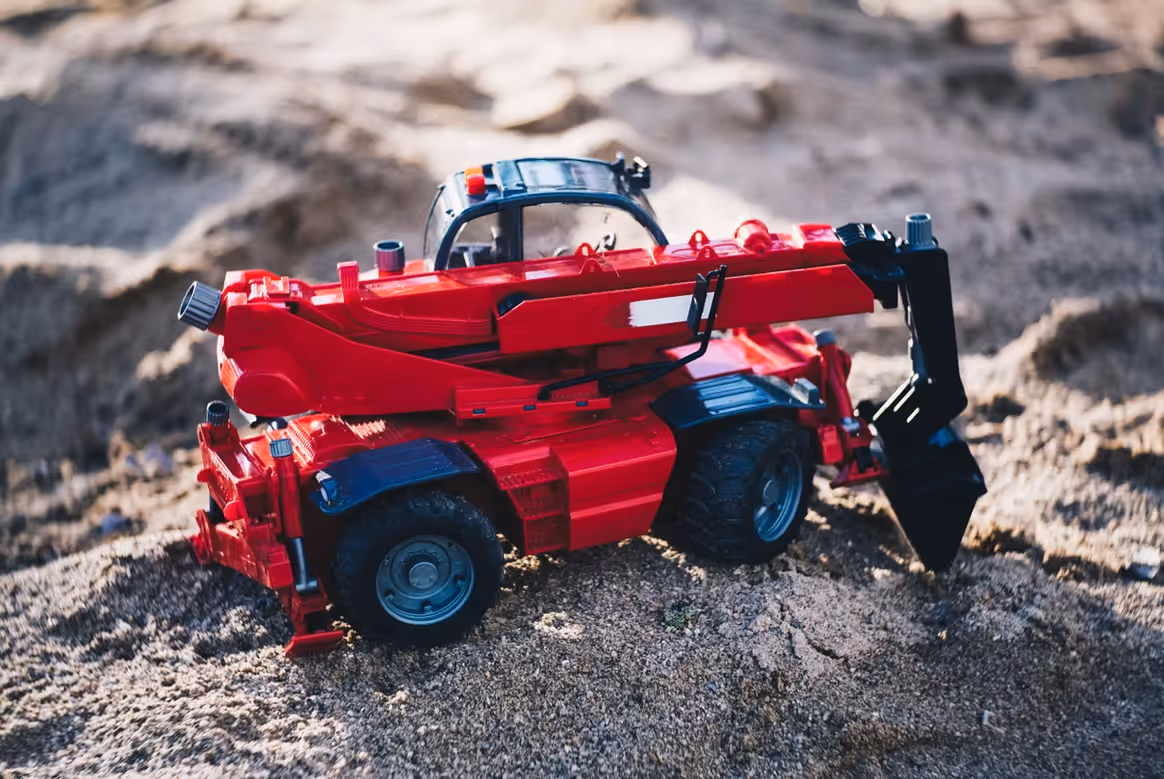 Rotes Spielzeug-Baggerfahrzeug mit Schaufel auf Sandboden.
