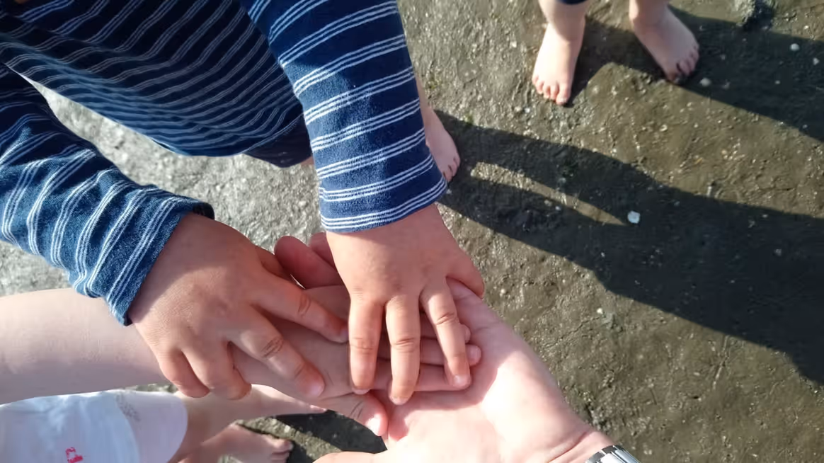 Kinderhände legen sich auf eine erwachsene Hand. Im Hintergrund ist das Wattenmeer