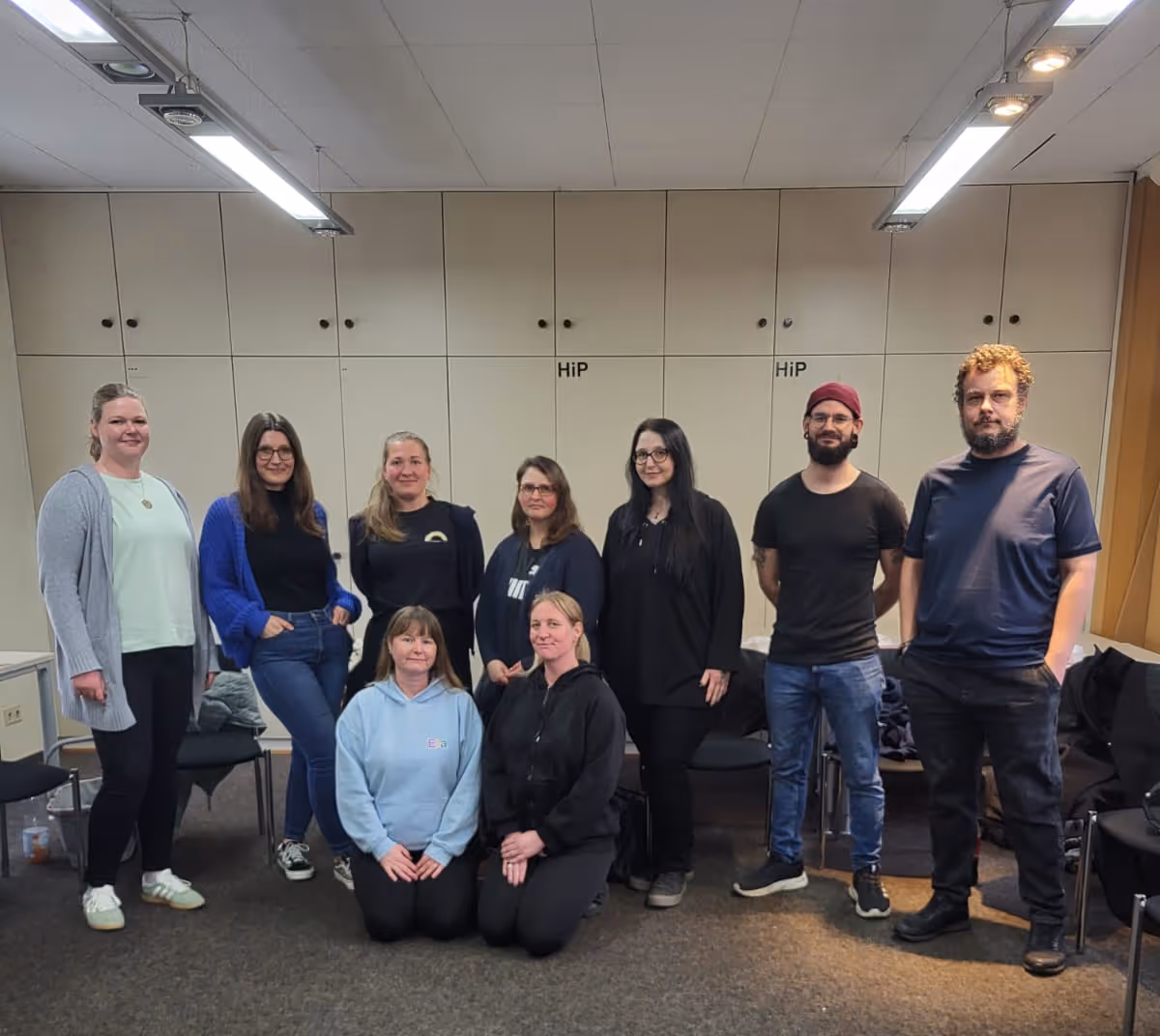 neun Personen von dem Kindertagespflege Verein posieren in einem Raum mit hellen Schränken.