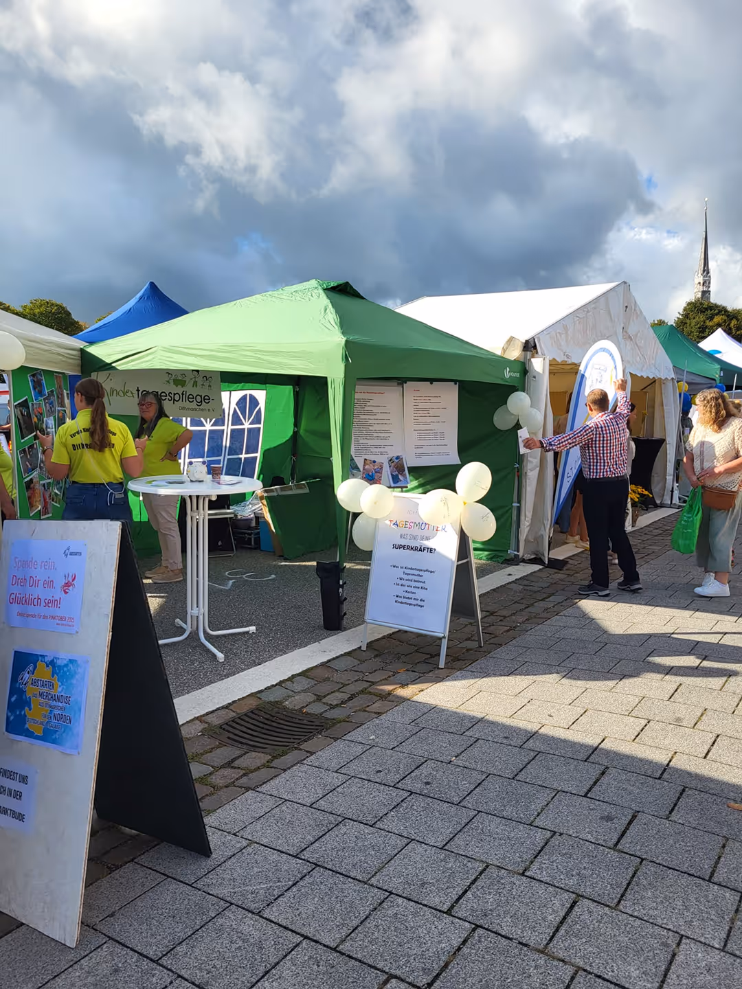 Menschen besuchen Informationsstände unter bunten Zelten bei einer Veranstaltung.