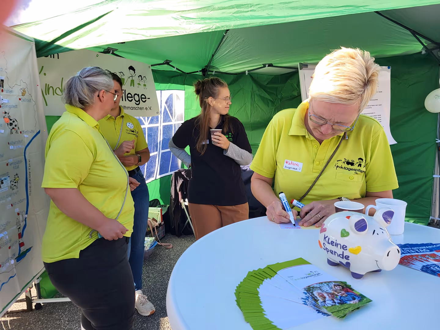 Drei Frauen von der Kindertagespflege in einem grünen Zelt bei einer Informationsveranstaltung.