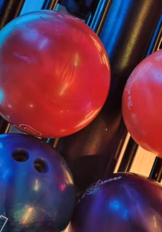 Verschiedene bunte Bowlingkugeln in einem Ablagegestell in einer Bowlingbahn.