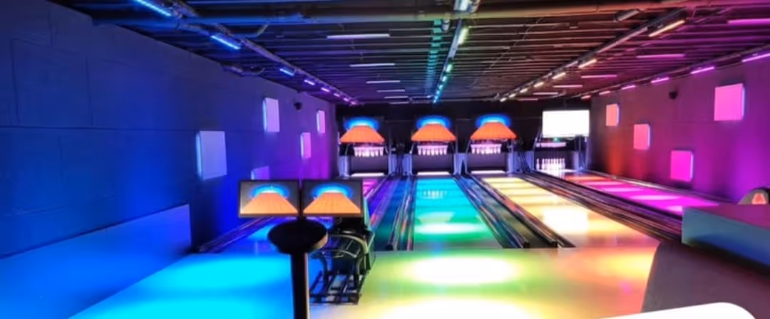 Hell beleuchtete Bowlingbahn mit vier Bahnen und buntem LED-Licht.