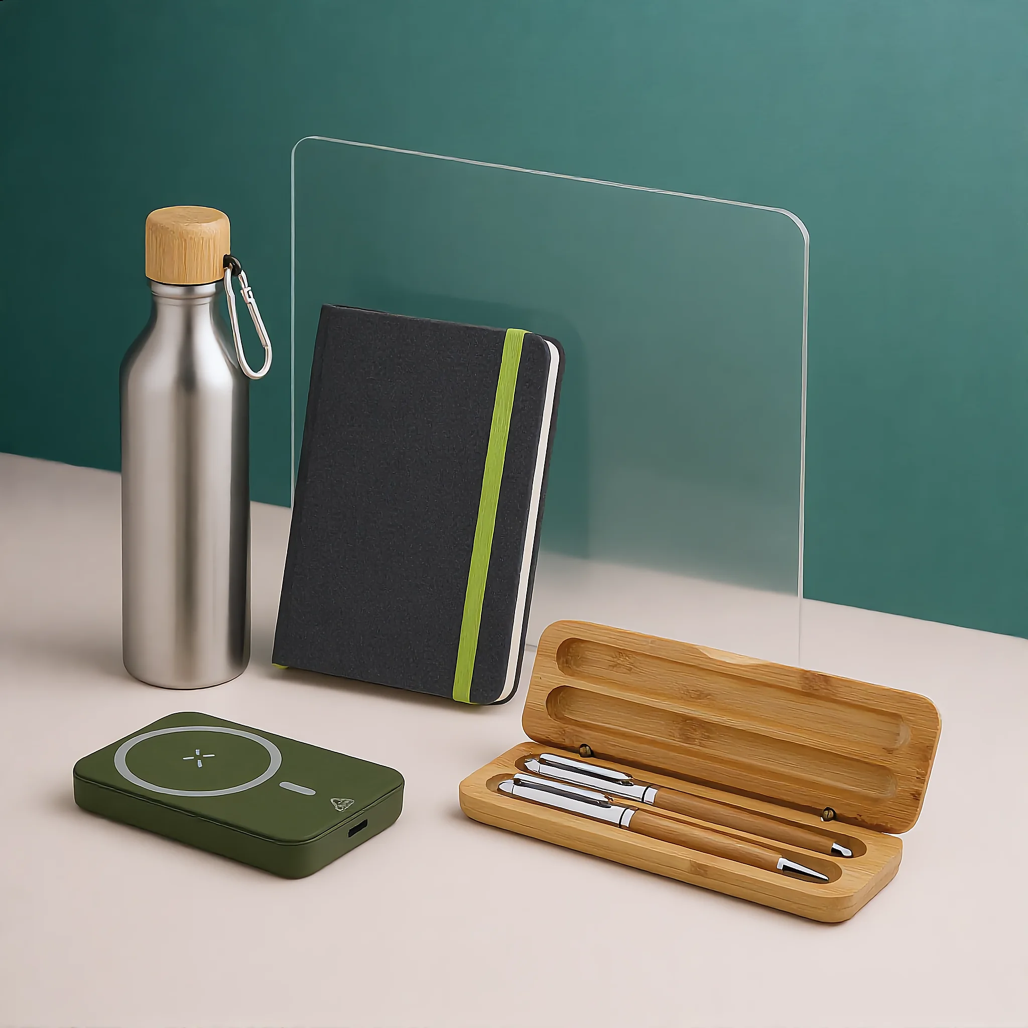 Ensemble personnalisé d’objets de bureau écologiques incluant une bouteille en acier inoxydable avec bouchon en bois, un carnet noir avec élastique vert, une boîte en bambou avec stylo et stylo plume, et un chargeur sans fil vert.