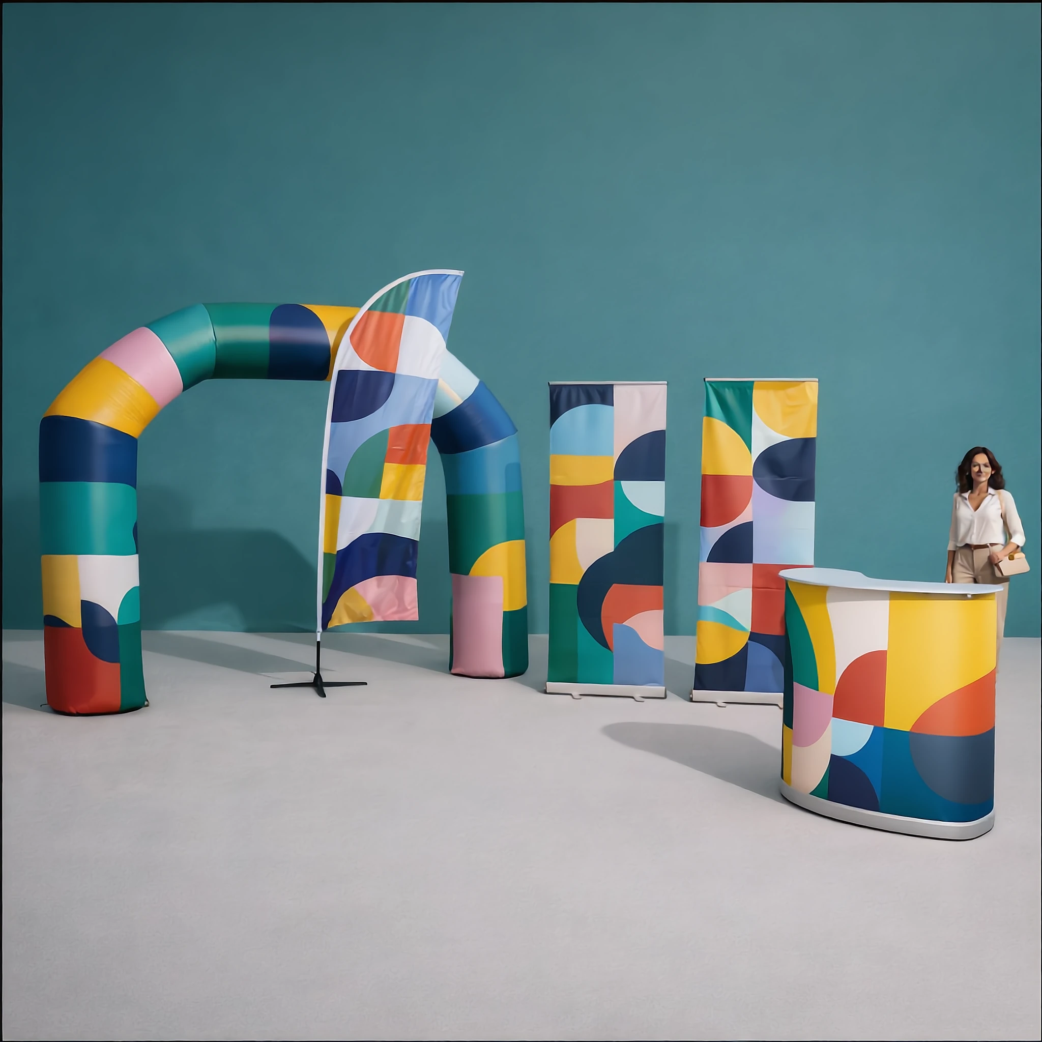 Stand d'exposition avec arche gonflable, drapeau, bannières et comptoir à motifs géométriques colorés, femme debout en arrière.