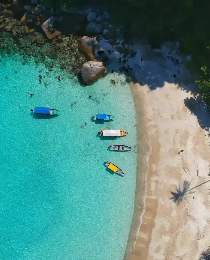 Image vue de haut d'une plage avec eau turquoise et sable blanc avec des bateaux 