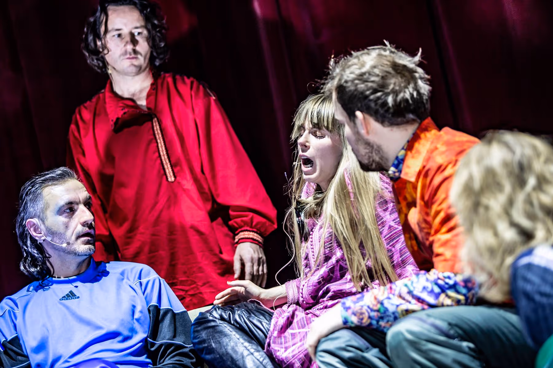 Four actors engaged in an intense theatrical scene with dramatic expressions and colorful costumes on stage.