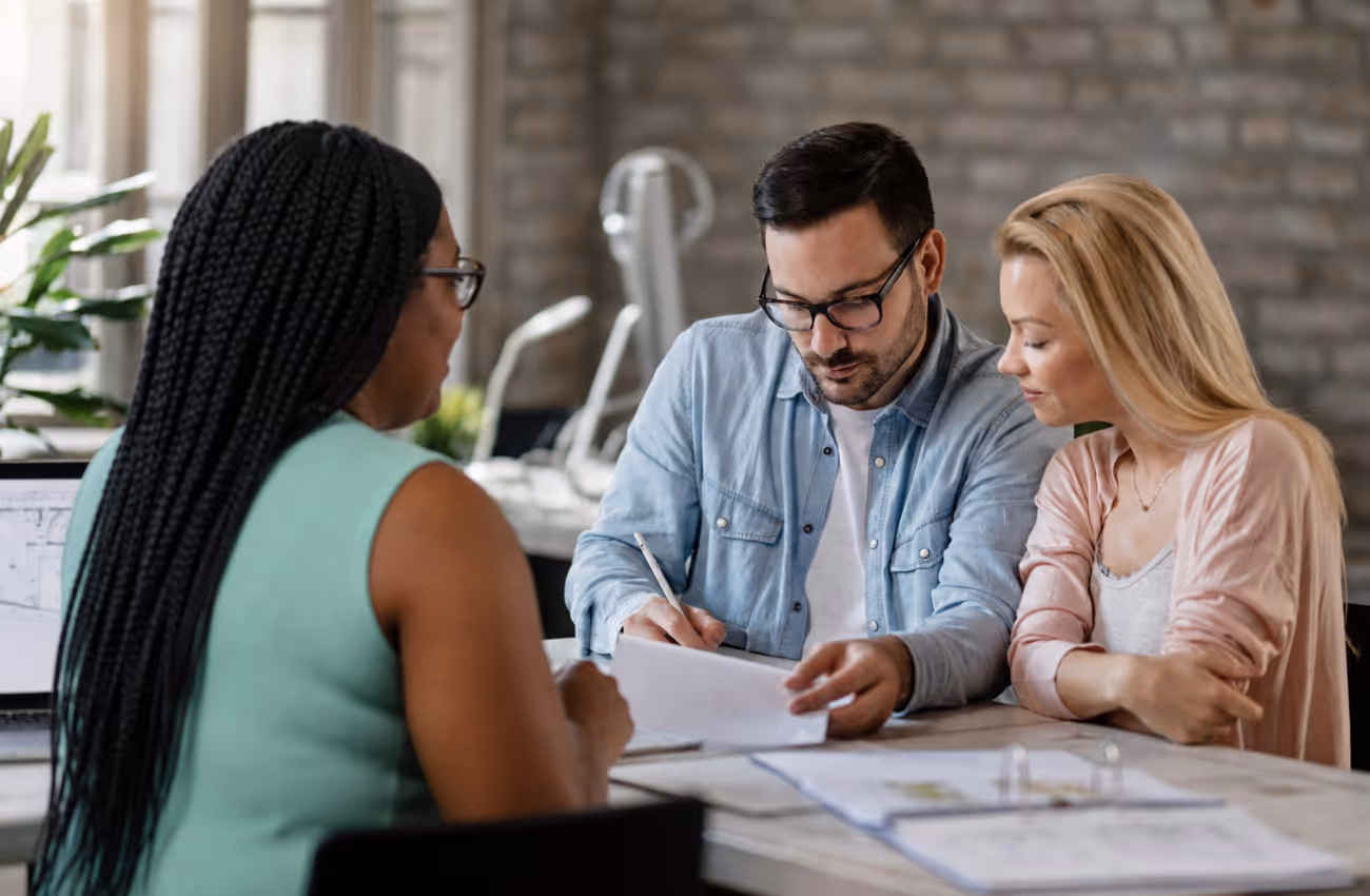 Insurance agent Krishna Drummonds meeting with a couple in a modern office to review policy documents and discuss personalized coverage options.