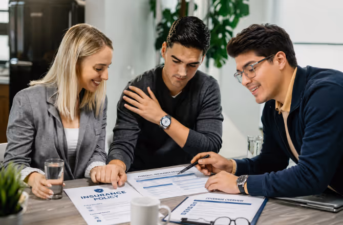 Alonso Contreras reviewing policy documents with a young couple during a consultation in a modern office, explaining coverage options and personal insurance details.