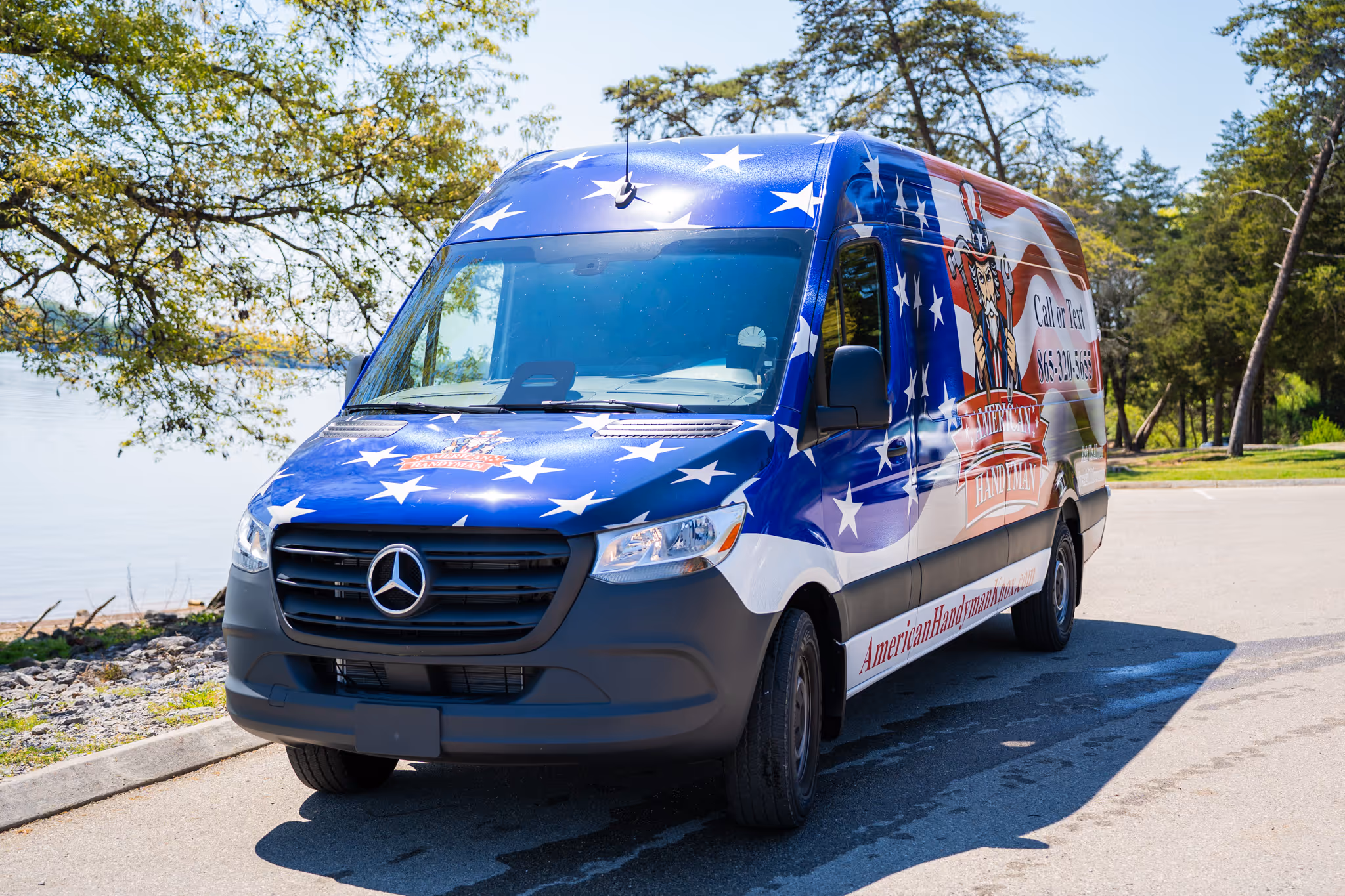 Mercedes-Benz van wrapped with American flag design and American Handyman logo parked near a lakeside.
