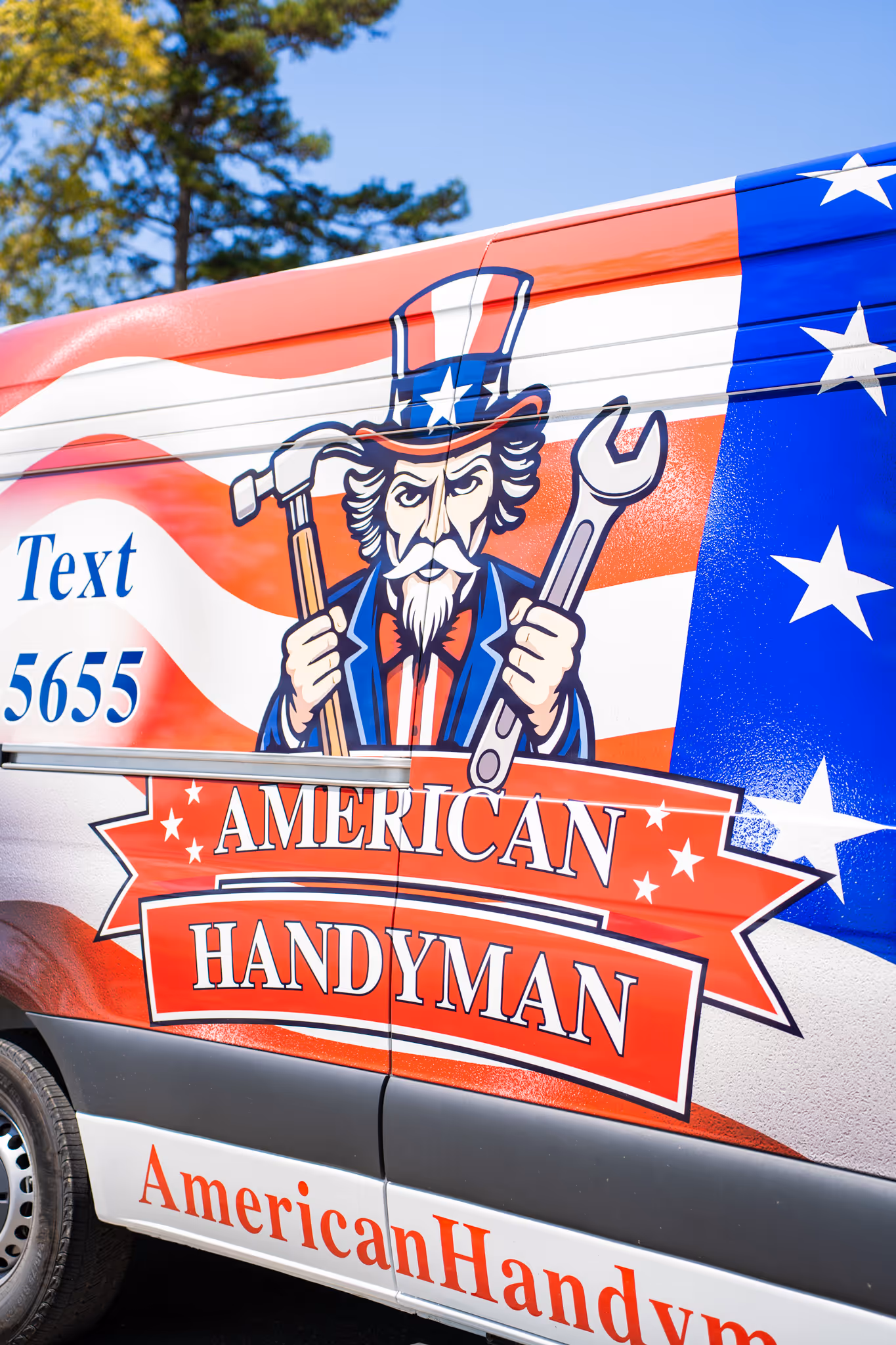 Side of a van with American Handyman branding showing an Uncle Sam figure holding a hammer and wrench, with a red, white, and blue flag background and text to text 5655.