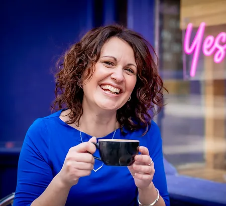 An image of Davina outside a cafe holding a mug.