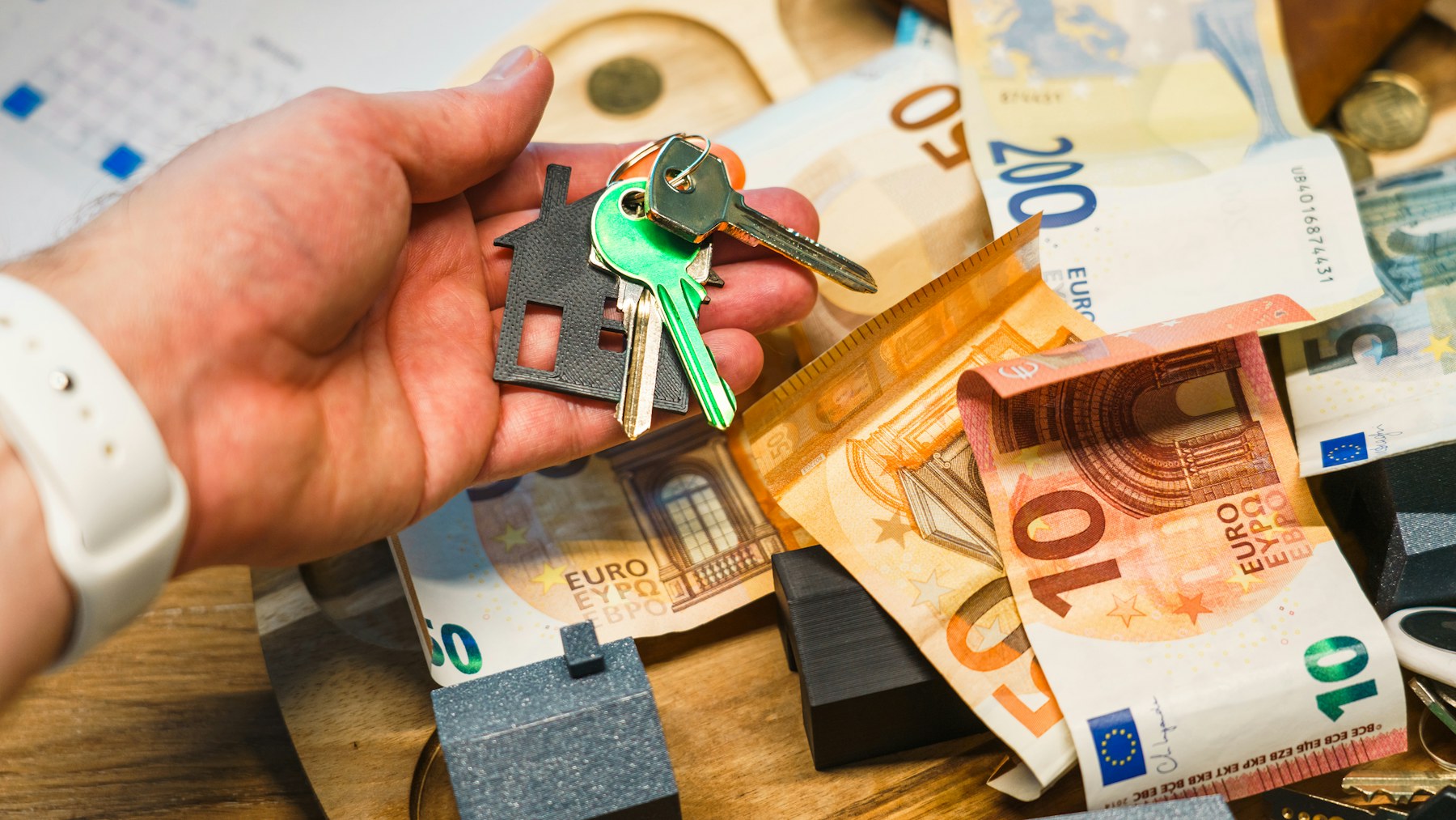 Hand hält Hausschlüssel über Euro-Geldscheinen