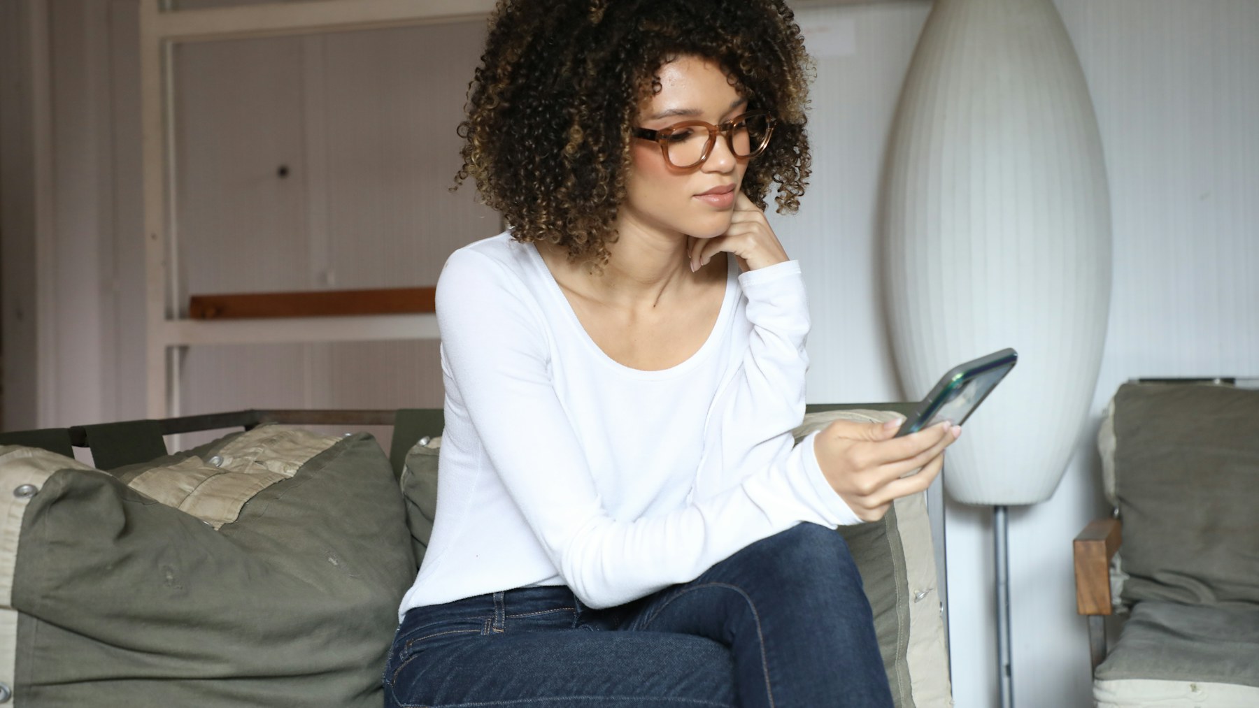 Frau sitzt auf dem Sofa und schaut nachdenklich auf ihr Smartphone