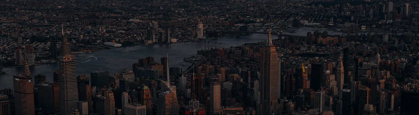 Aerial view of a city skyline at dusk with tall skyscrapers and a river in the background.