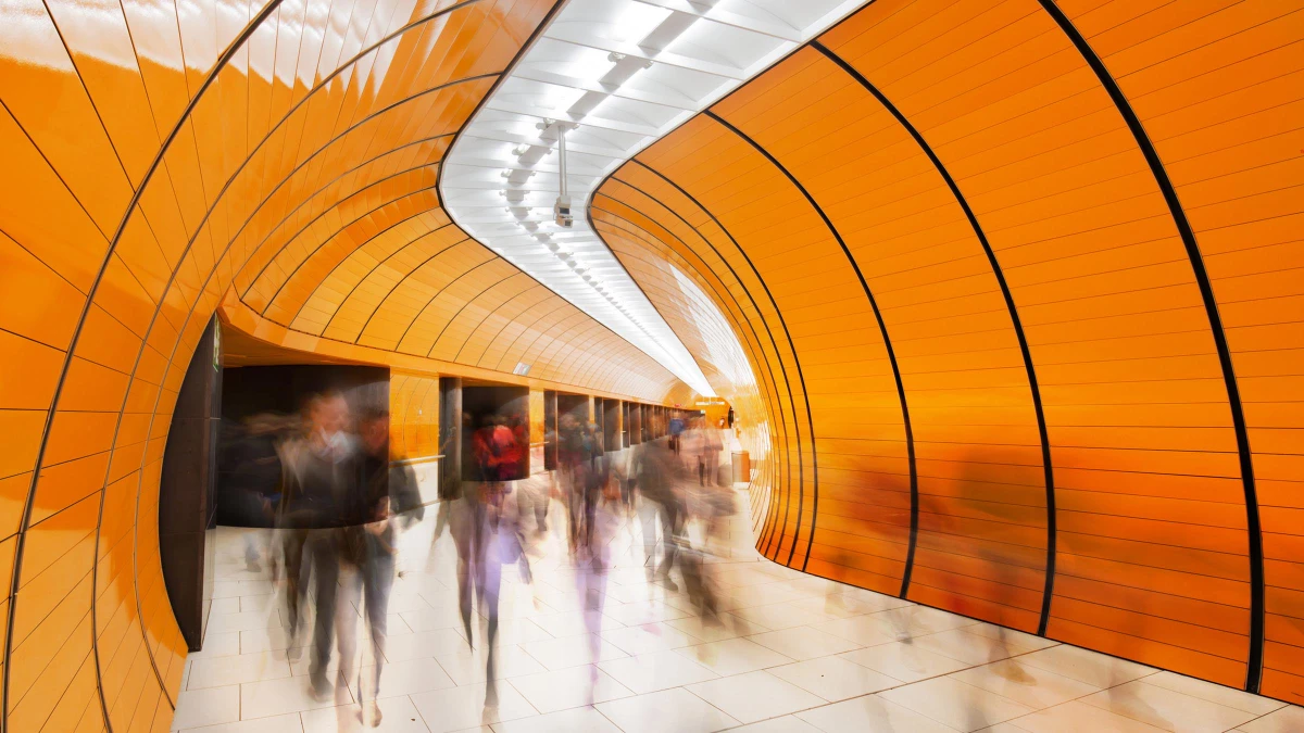 Crowd walking through a brightly lit modern subway tunnel with curved orange walls.